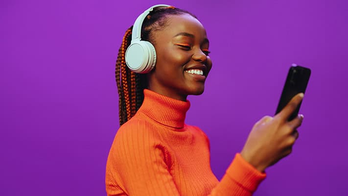 Woman in an orange sweater smiling at her smartphone