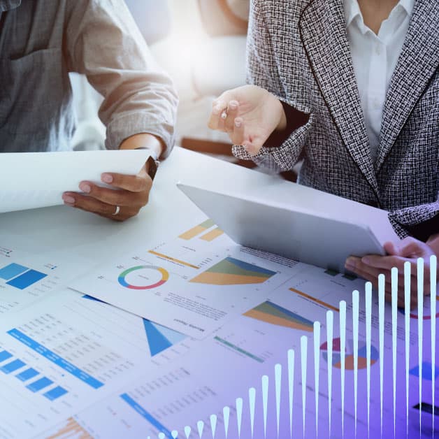 Closeup of two people working at a table with graphs spread out on it