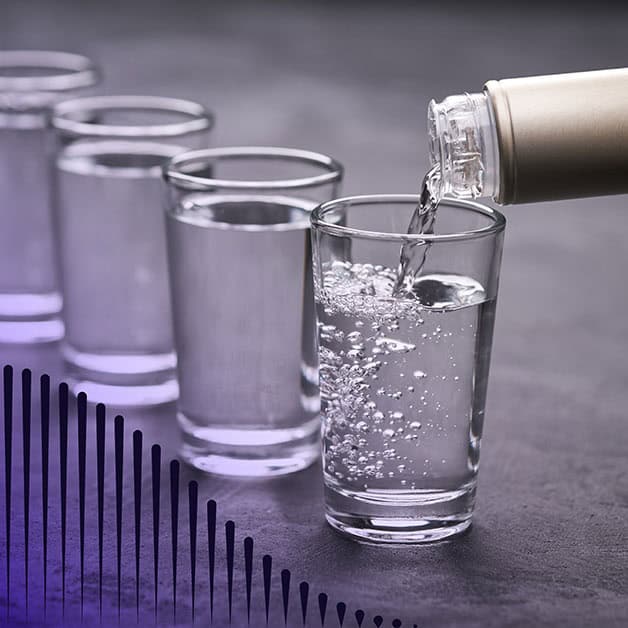 Row of shot glasses with vodka being poured into them