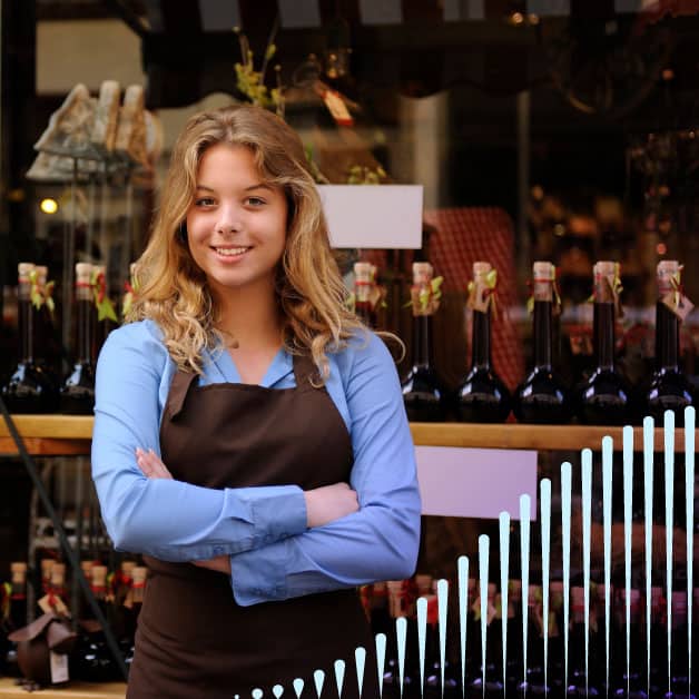 Woman with apron smiling in front of alcohol bottles with her arms crossed