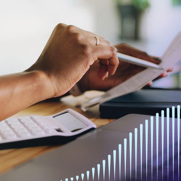 Closeup of hand pointing a pen at a piece of paper on a crowded desk