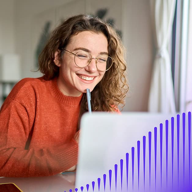 Women with glasses smiling at her laptop with a pen in her hand